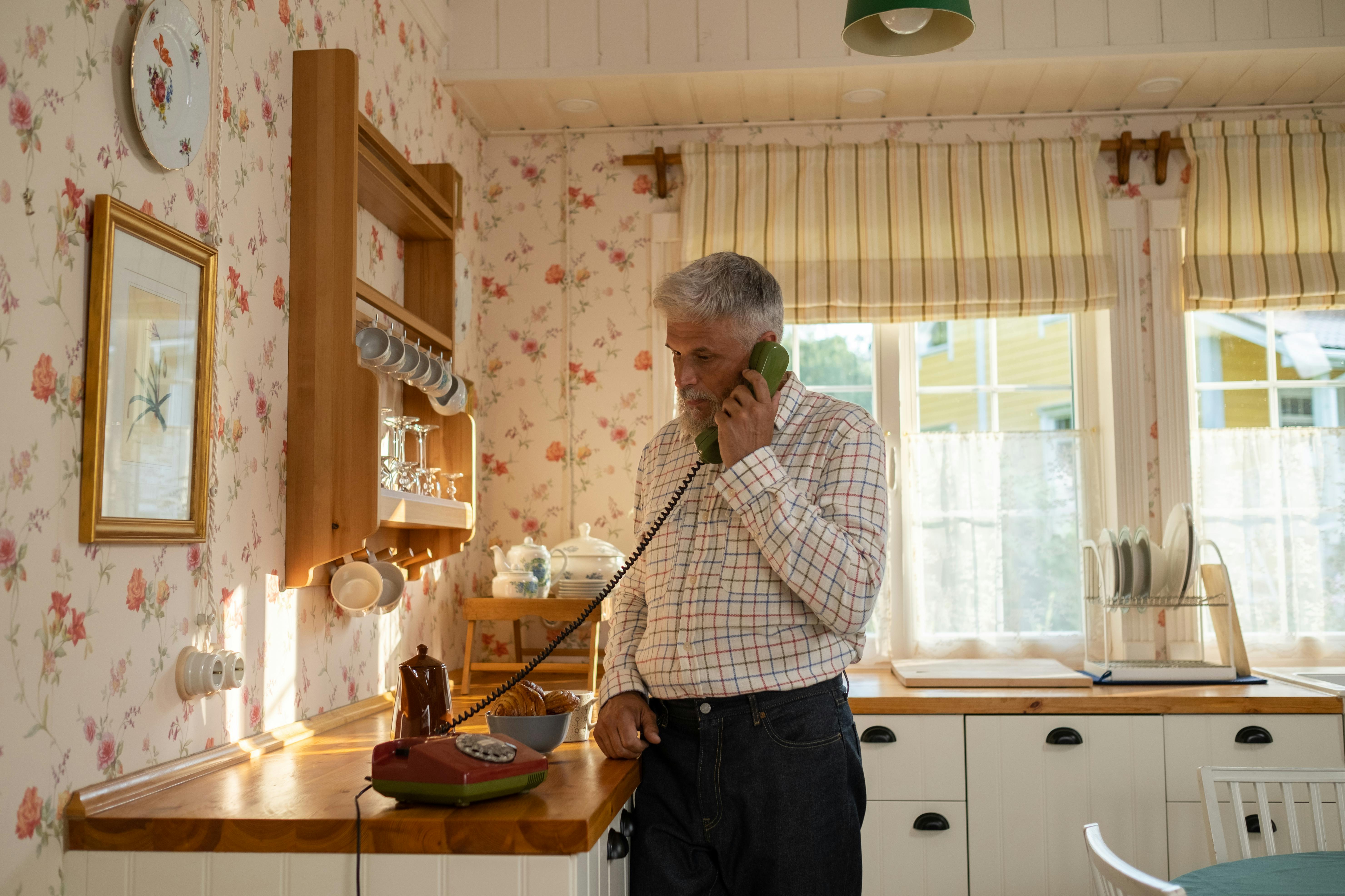 Senior holding landline telephone in cottage kitchen
