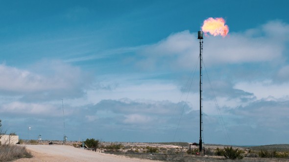 Methane flame flare in an oil field against a partially cloudy sky