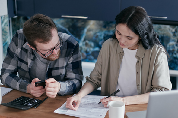 Two people sit at a table looking at a bill, calculator and coffees on the table