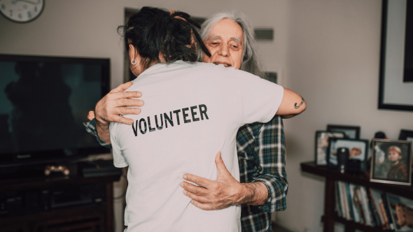 Senior hugging volunteer at home