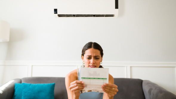 Woman holding energy bill looking confused on couch