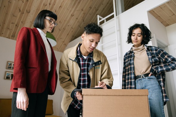 Two people watch as one person signs a contract on a moving box