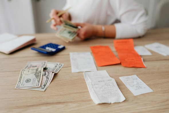 Receipts and cash in front of hands counting money with a calculator