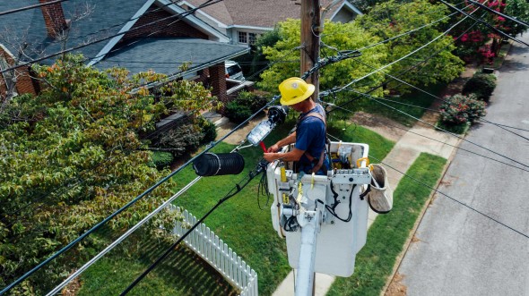 Man working on powerline against green lawn and house