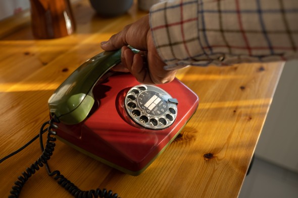 Hand picking up a landline rotary phone on a wood table
