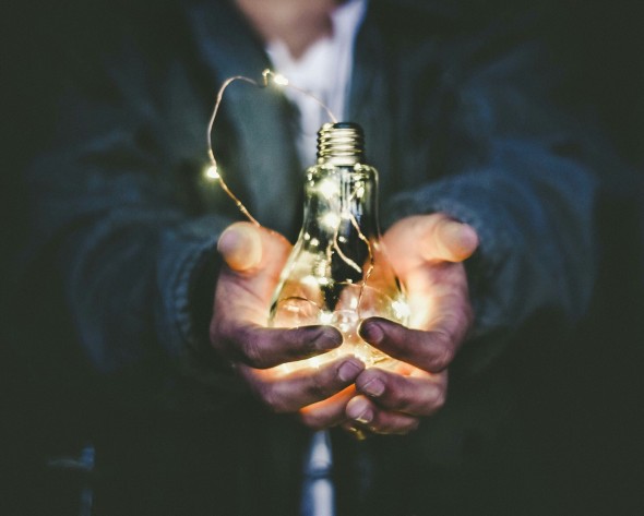 Hands holding a lit light bulb 