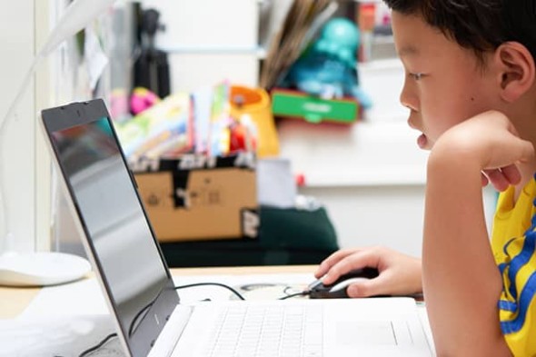 Child sits at a laptop while using the mouse.