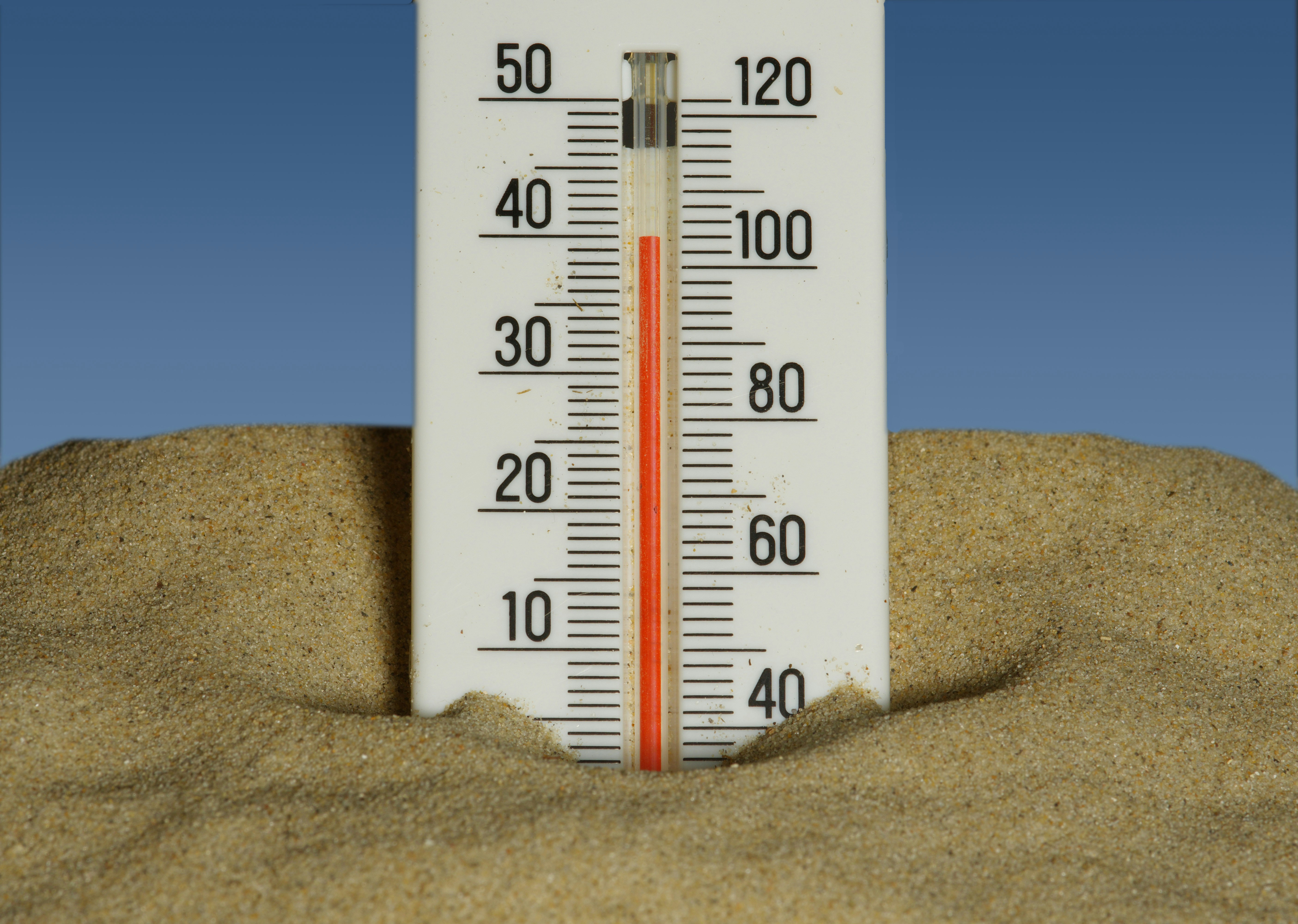 Thermometer on sand and blue background